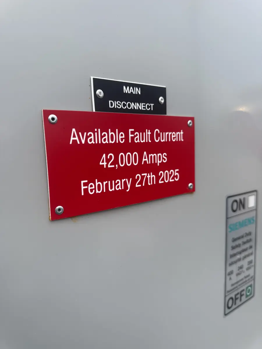 Red engraved Available Fault Current label with white text on switchgear next to the main disconnect
