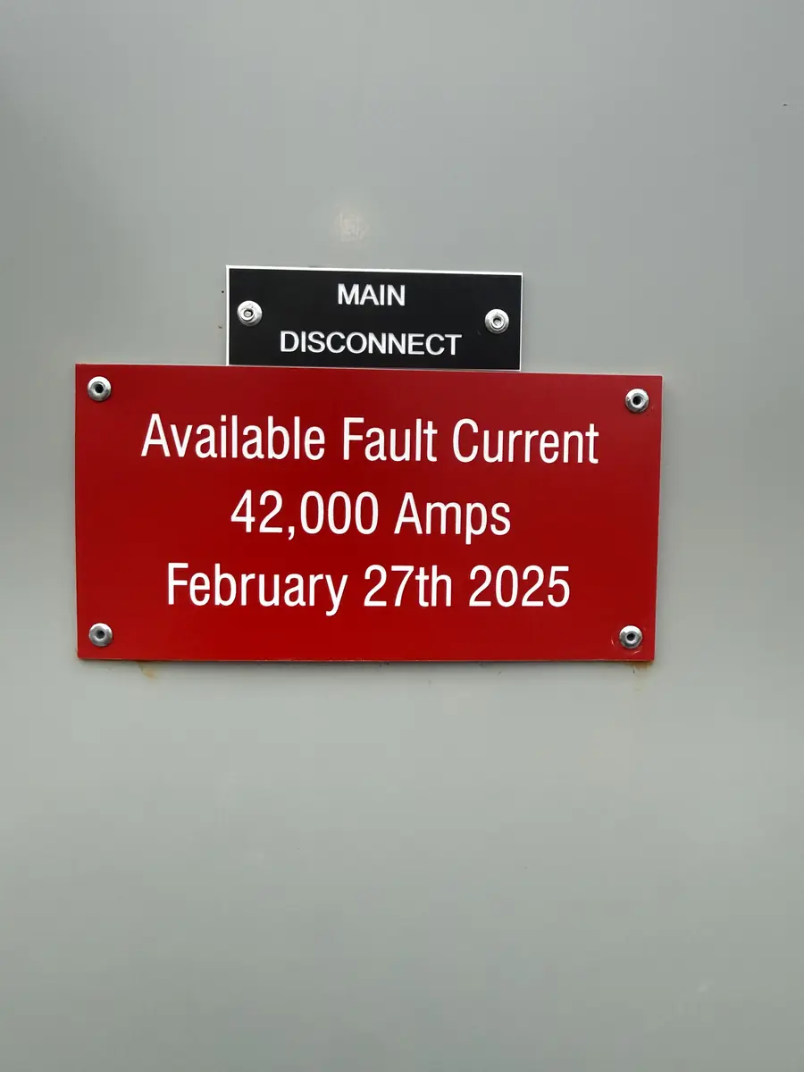 Black MAIN DISCONNECT tag above a red Available Fault Current label on a gray switchgear door