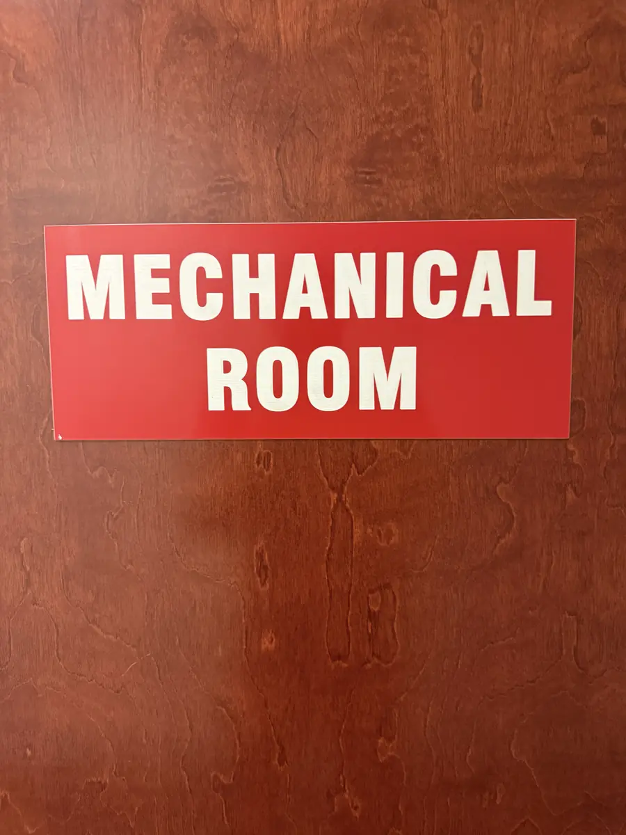 Red engraved MECHANICAL ROOM sign with white letters on a wood door