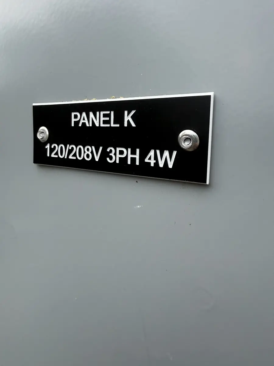 Black engraved nameplate reading PANEL K 120/208V 3PH 4W mounted with two screws