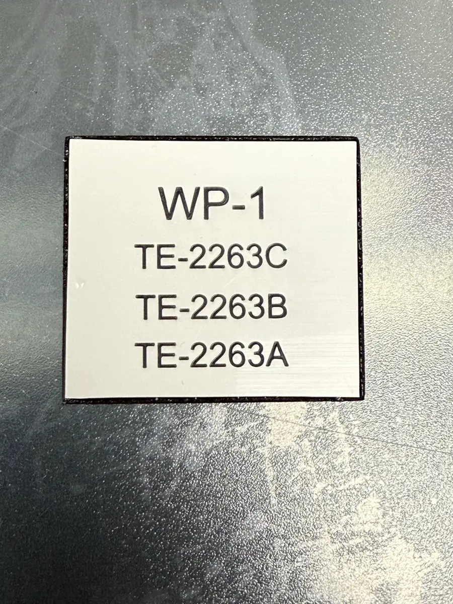 White phenolic tag laser-engraved with black text WP-1 and three TE-2263 circuit lines